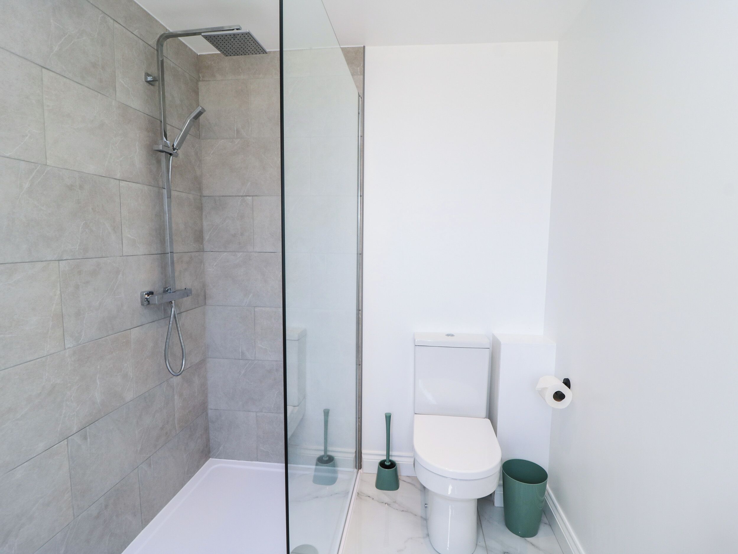 Un baño moderno con cabina de ducha de vidrio, inodoro y cubo de basura.