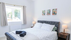 A bedroom with a bed, a window with curtains, a bedside table with a lamp, and three framed pictures on the wall. - Cern-wyn (Chippenham)