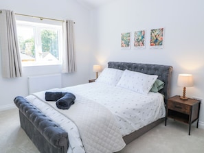 A bedroom with a bed, a window with curtains, a bedside table with a lamp, and three framed pictures on the wall.