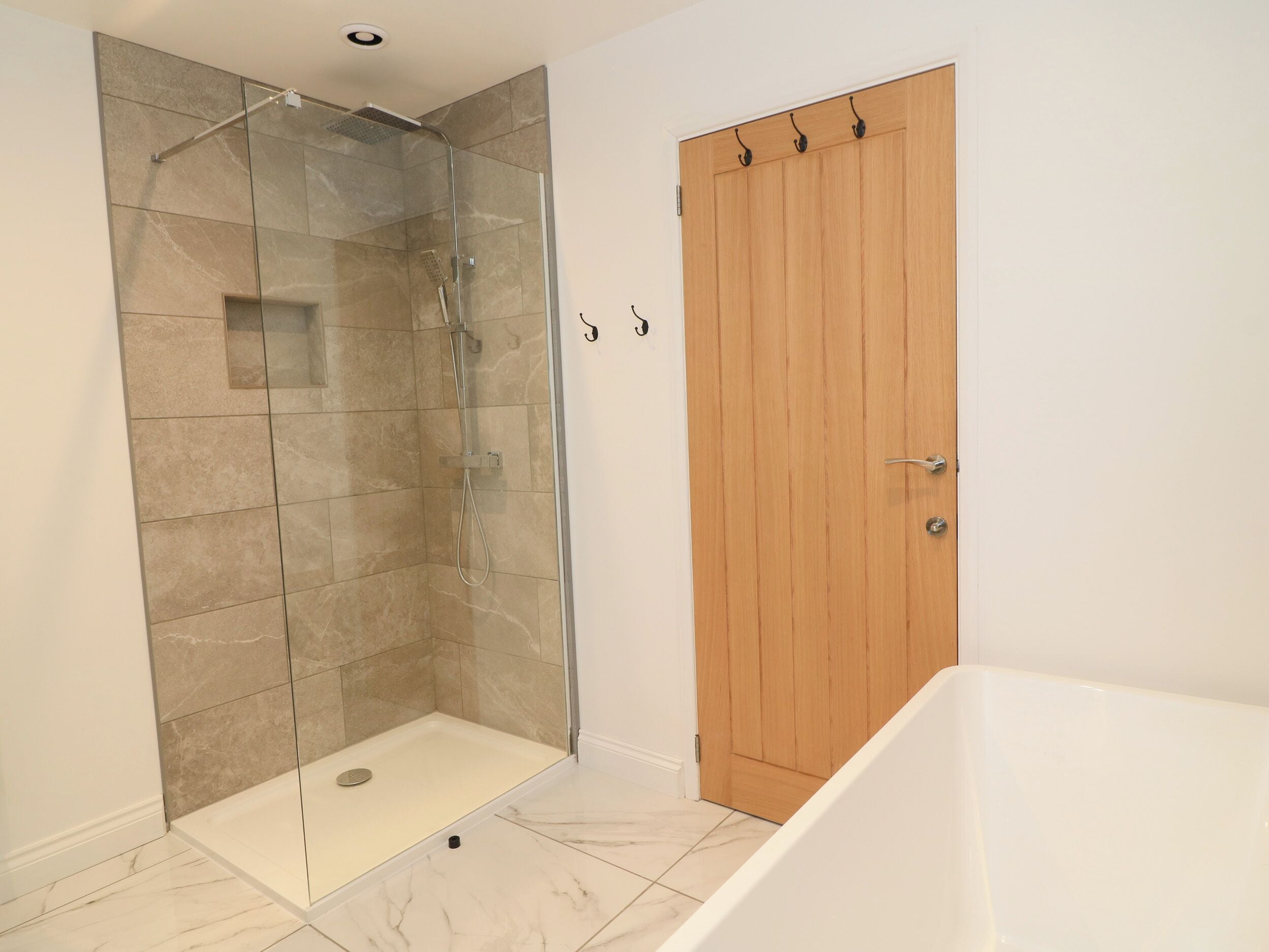 A bathroom with a glass-enclosed shower, a wooden door, and a white bathtub.