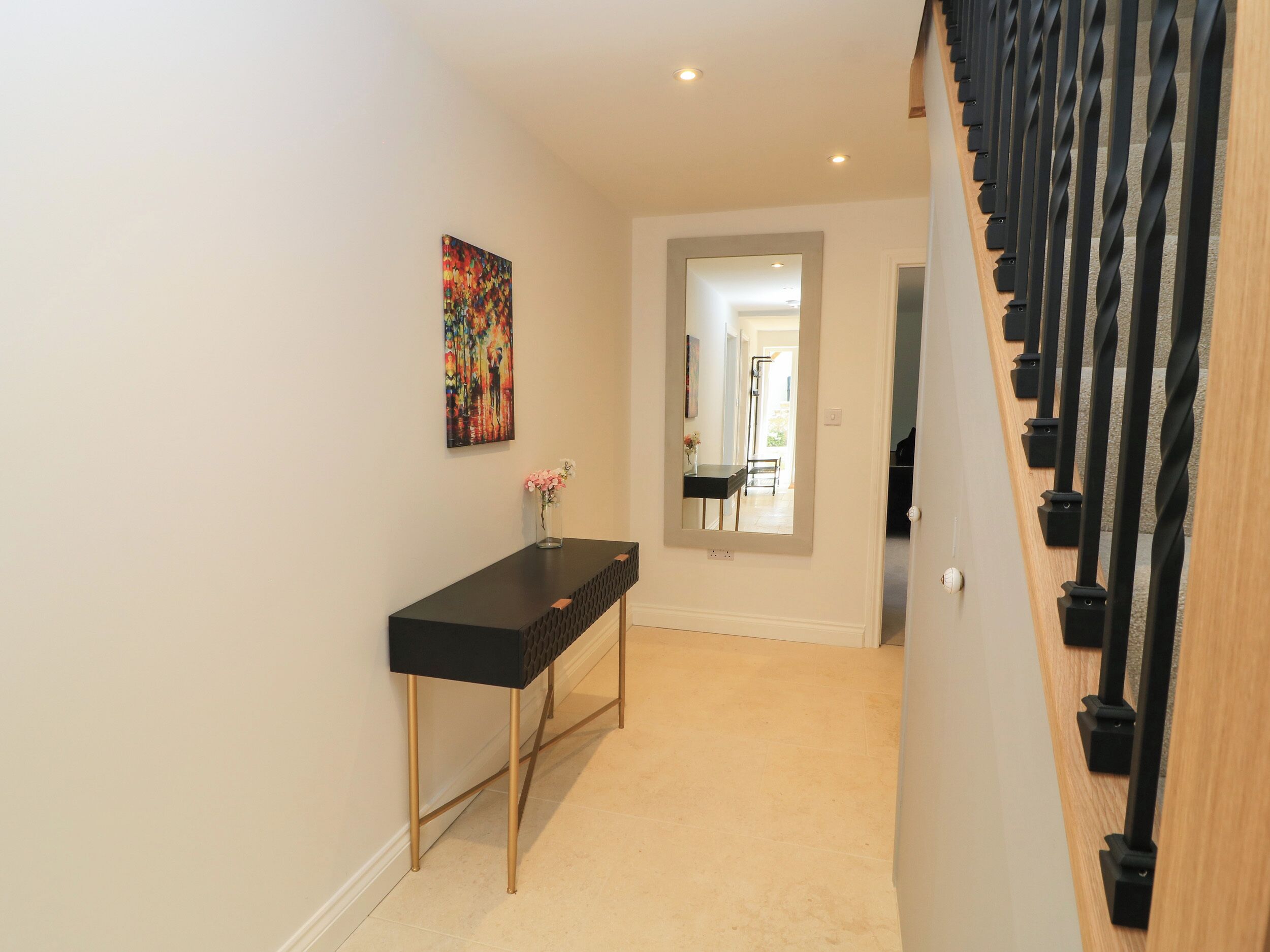 A hallway with a black console table, a vase with flowers, and a staircase with black balusters.