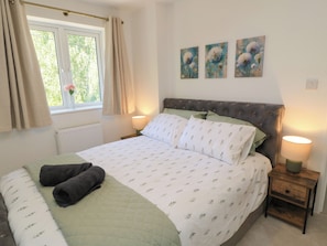 Un dormitorio con cama, una ventana con cortinas, un radiador y tres cuadros colgados en la pared.