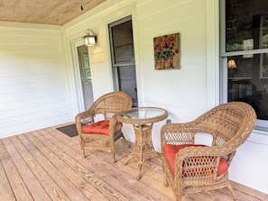 A covered porch with wicker furniture and a glass table, white siding walls, and a window with a view. - Crane Creek Vineyards- Cozy Vineyard Cottage (Young Harris)