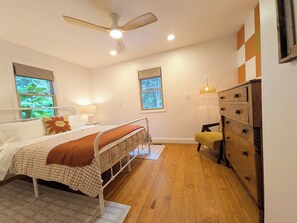 A bedroom with a bed, bedside tables, a dresser, a ceiling fan, and windows with views of greenery. - Crane Creek Vineyards- Cozy Vineyard Cottage (Young Harris)