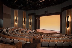 Un auditorio moderno con asientos escalonados, una pantalla grande y paneles de madera.