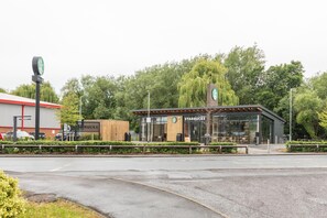 Un bâtiment moderne, avec une enseigne Starbucks, un parking et, au fond, un bâtiment avec un toit rouge.