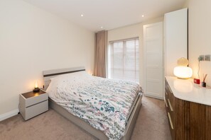 Une chambre à coucher comprenant un lit, une table de chevet, une commode, un meuble à tiroirs, un miroir et une fenêtre avec des stores.