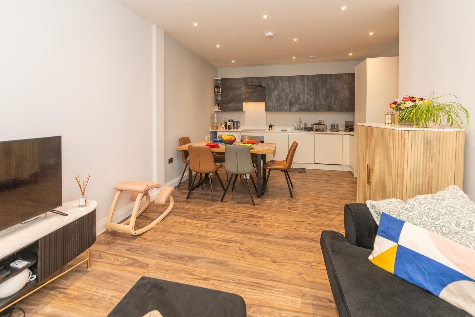 A modern living room with a flat-screen TV, a sofa, and a dining area with chairs and a table.