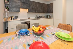 Une cuisine moderne avec un coin repas, comprenant une table dressée avec des assiettes, un panier de fruits et une machine à café.