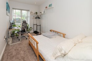 A bedroom with a bed, a desk with a chair, a window, and a shelf with items. - Brand-New Spacious Flat | For Business & Leisure - Pass the Keys (Reading)
