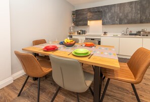 Un coin repas avec une table en bois, quatre chaises et un saladier rempli de fruits.