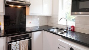 A modern kitchen with white cabinets, a stainless steel range hood, a built-in oven, a dishwasher, and a washing machine. - Bright, Leafy Oasis in South London - Pass the Keys (London)