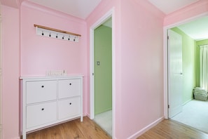 Ein Zimmer mit rosafarbenen Wänden, einem weißen Schminktisch, einem hölzernen Kleiderständer und einer grünen Tür.
