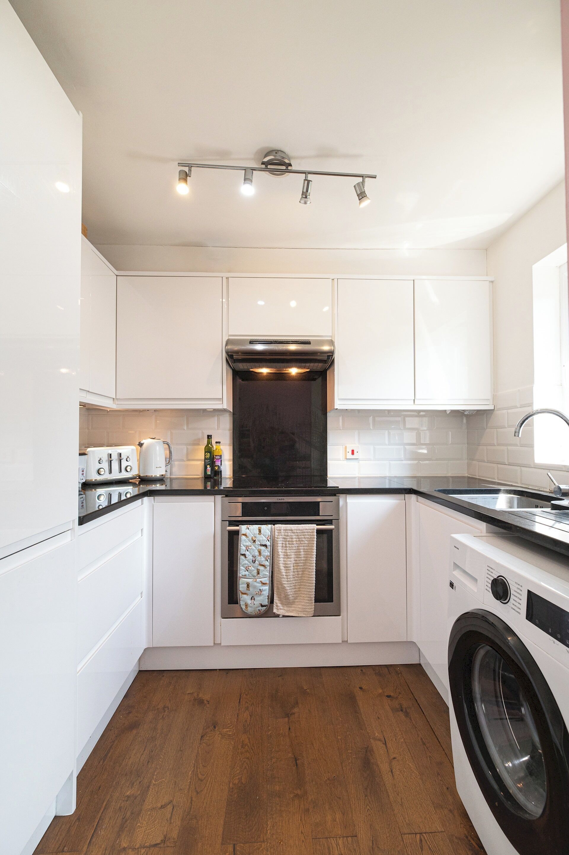A compact kitchen with white cabinets, a built-in oven, a washing machine, and a coffee maker.