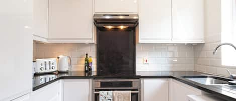 A compact kitchen with white cabinets, a built-in oven, a washing machine, and a coffee maker.
