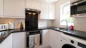 A compact kitchen with a built-in oven, a microwave, a sink, and a washing machine. - Bright, Leafy Oasis in South London - Pass the Keys (London)