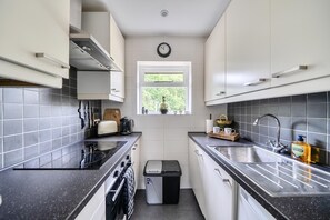 A modern kitchen with white cabinets, a black countertop, a window, and a trash bin. - Bright Esher Home with Free Parking - Pass the Keys (Esher)