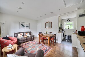 Ein Wohnzimmer mit einer Couch, einem Esstisch mit Stühlen, einem gemusterten Teppich und einer Küchenzeile mit einem Fenster.