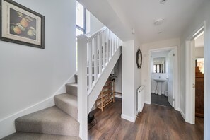 Eine Treppe mit Teppichstufen führt zu einem Holzgeländer, eine weiße Wand mit einem gerahmten Bild und ein Flur mit Holzboden und einer weißen Tür.