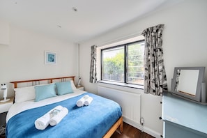 Ein Schlafzimmer mit einem Bett, einem Fenster mit Vorhängen, einem Nachttisch mit Lampe und einer Heizung.