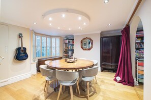 A dining area with a round wooden table, grey chairs, a guitar on the wall, and a bookshelf. - Stylish Stockwell House with Garden & Comfort  - Pass the Keys (London)
