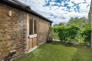 A brick house with a wooden door, a small garden with grass and trees, and a clear sky. - Stylish Stockwell House with Garden & Comfort  - Pass the Keys (London)
