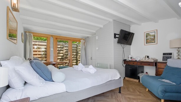 Ein Hotelzimmer mit Bett, Schreibtisch, Stuhl, Fernseher und einem Fenster mit Blick auf Grünflächen.