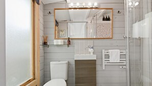 Ein Badezimmer mit Toilette, Waschbecken, Spiegel, Dusche und einem Fenster.