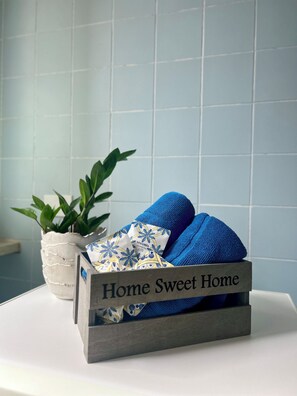 Ein Badezimmer mit einem weißen Waschbecken, einer Topfpflanze und einer Holzkiste mit der Aufschrift 'Home Sweet Home', die blaue Handtücher enthält.