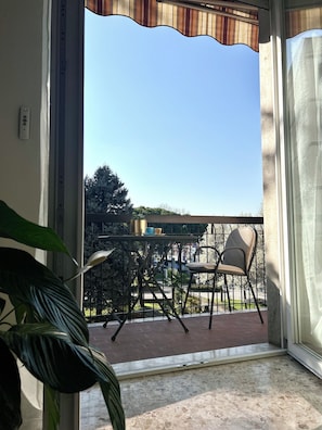 Ein Balkon mit einem Stuhl, einem Tisch, einem Blumentopf und Blick auf Bäume sowie ein Gebäude in der Ferne.