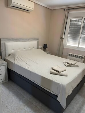 Ein Schlafzimmer mit Bett, Nachttisch, Lampe und einem Fenster mit Jalousien.