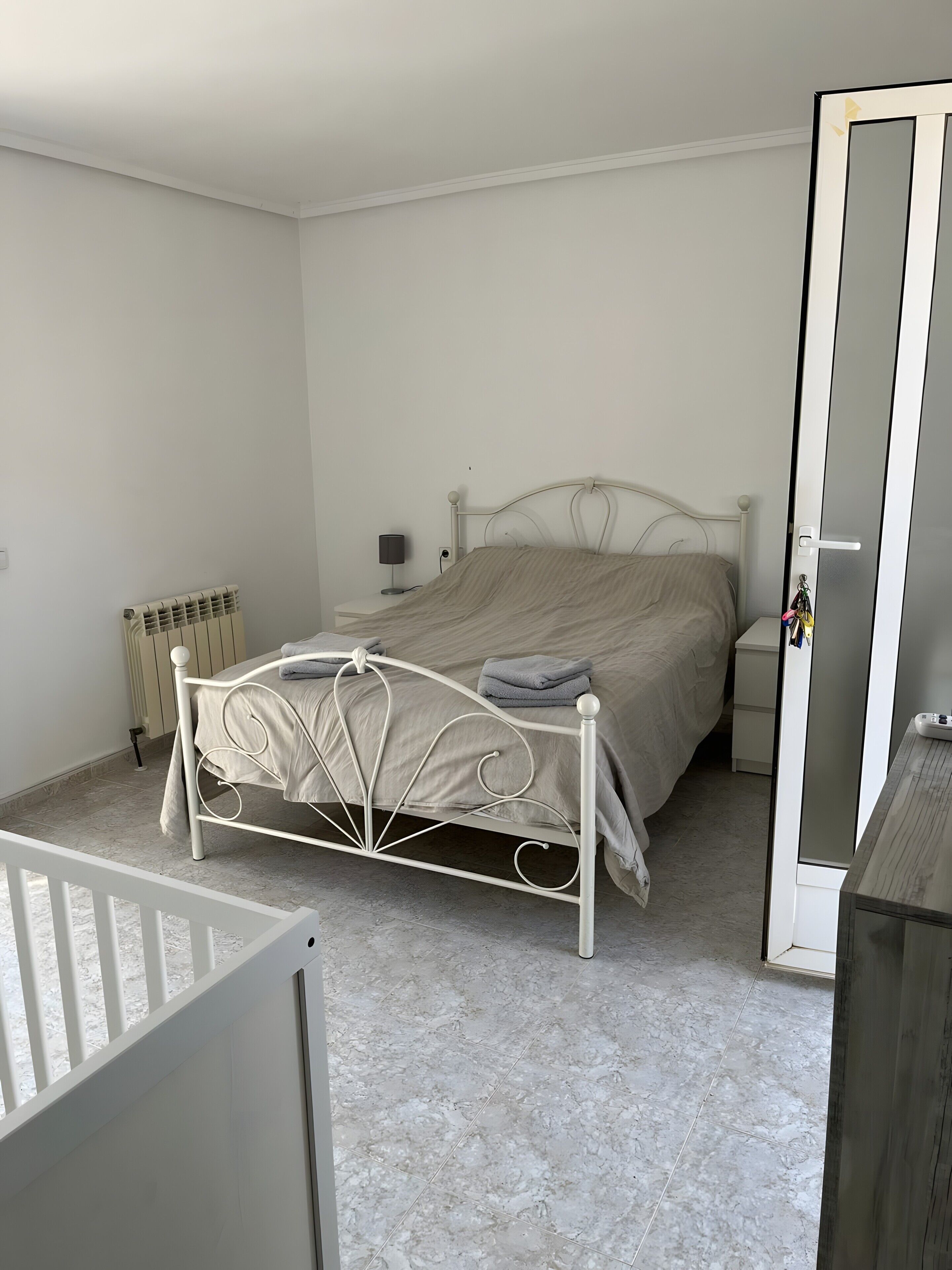 Un dormitorio con cama, mesita de noche, lámpara y radiador.