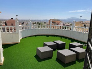 A rooftop terrace with artificial grass, wicker furniture, and a white balustrade overlooking a cityscape. - Villa 'Casa Familia Thijssen' with Private Pool, Wi-Fi and Air Conditioning (Mazarrón)