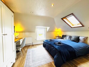 Een slaapkamer met een bed, bureau, stoel, radiator, raam en dakraam.