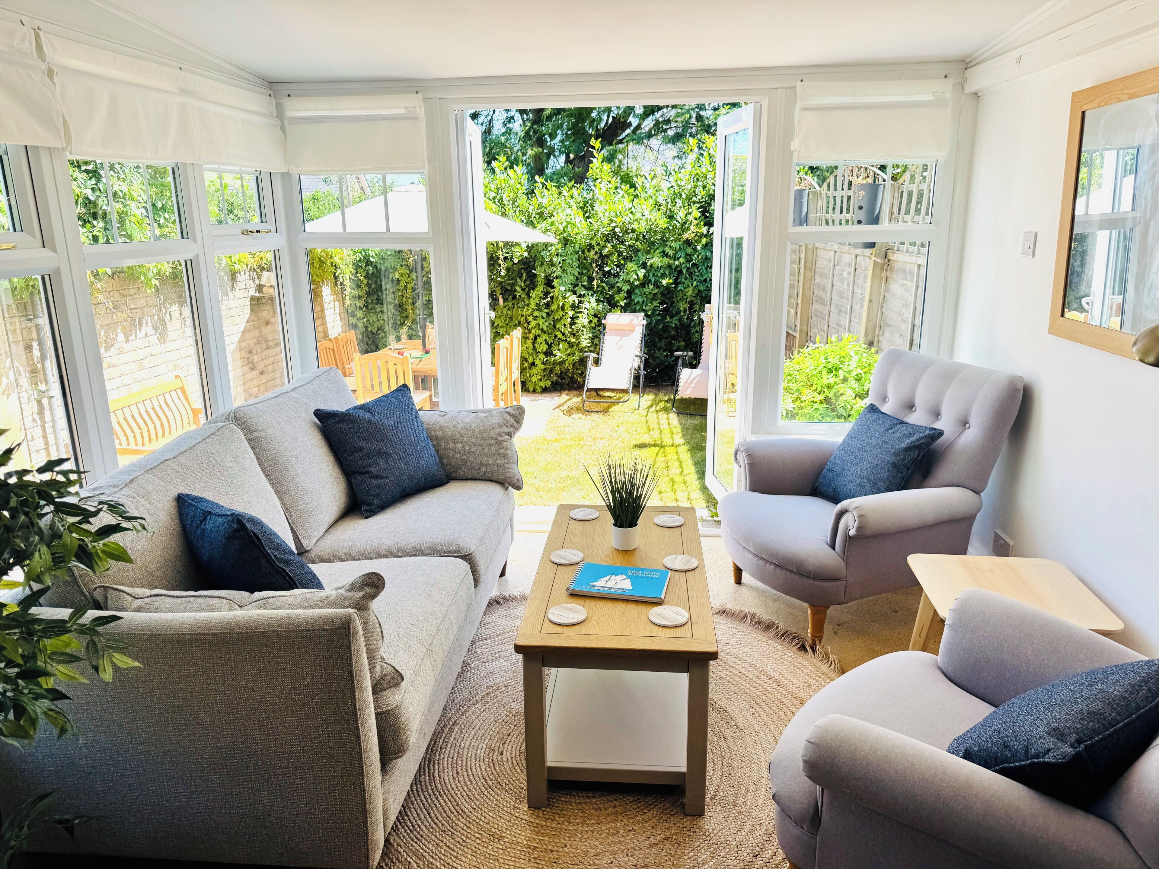 A conservatory with a sofa, armchair, and coffee table, and a view of a garden.