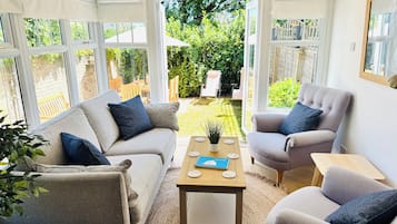 A conservatory with a sofa, armchair, and coffee table, and a view of a garden.
