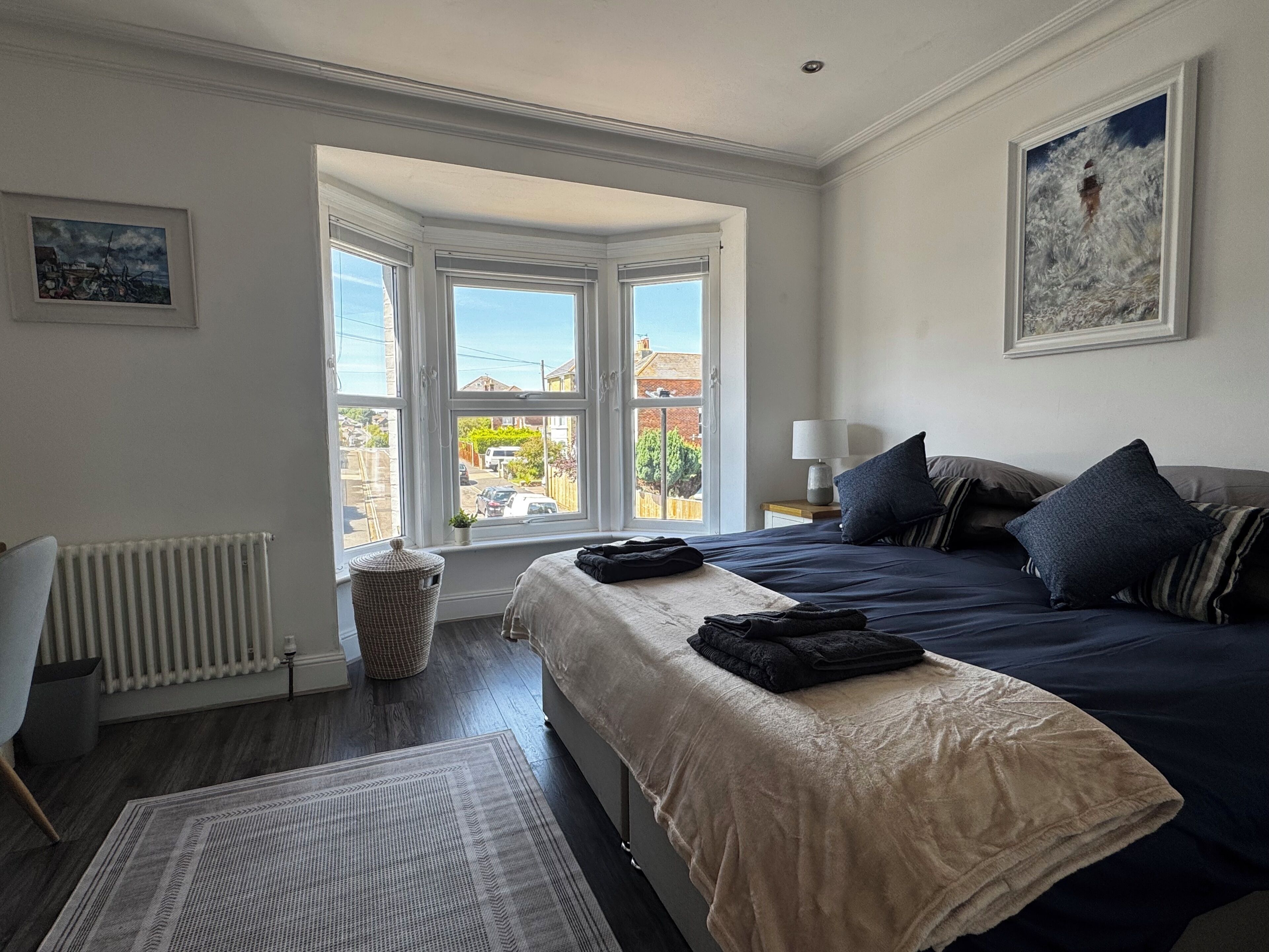 A bedroom with a large window, a bed, a bedside table, a lamp, and a radiator.
