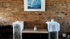A brick wall with a framed poster of a sailing ship, a coffee machine, a jar, and a table with a towel.