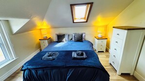 A bedroom with a bed, two bedside tables, a dresser, and a skylight.