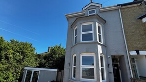 A two-story residential building with a bay window, a small porch, and a gravel driveway.