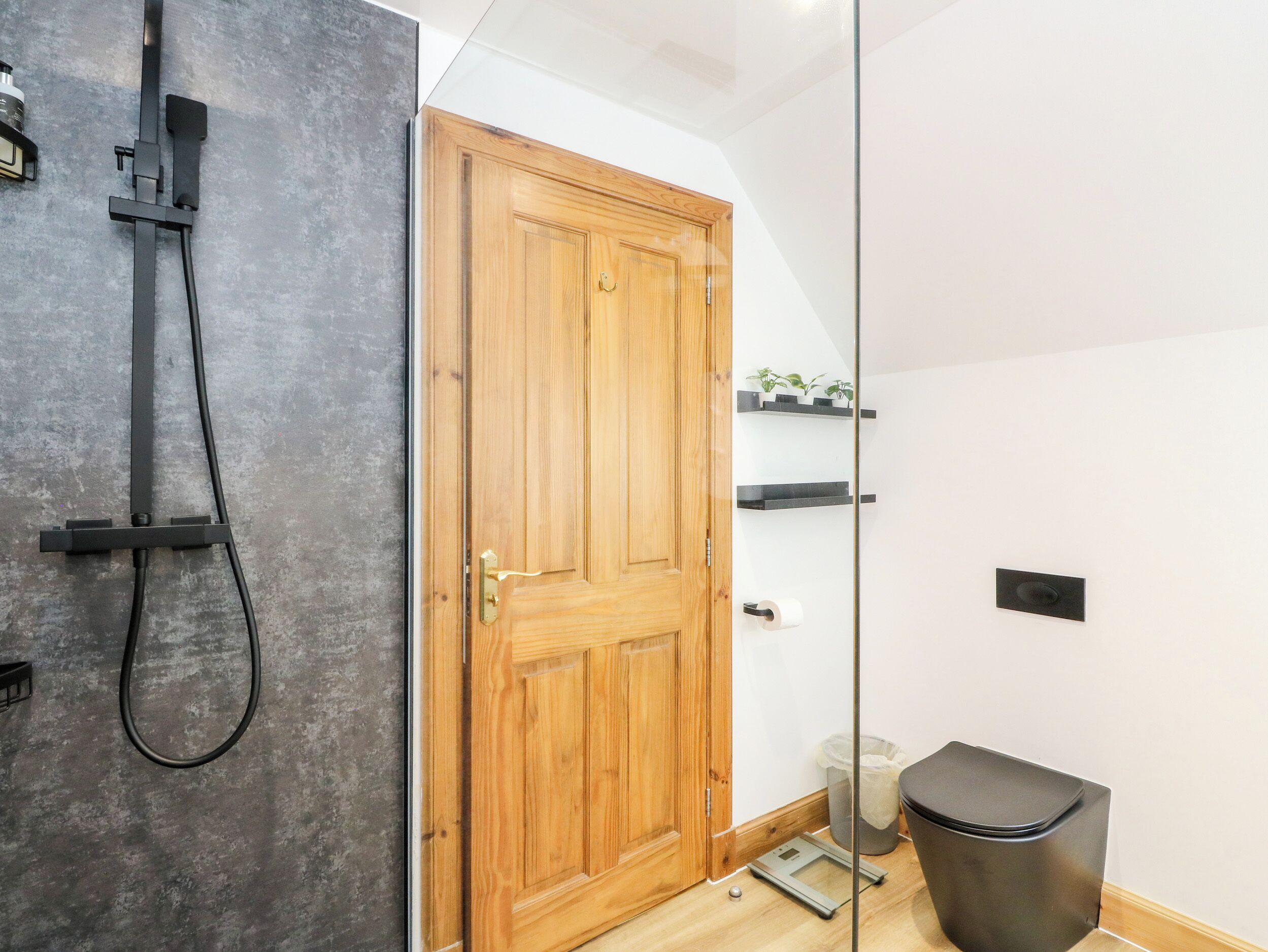 A bathroom with a wooden door, a shower, a toilet, and a trash bin.