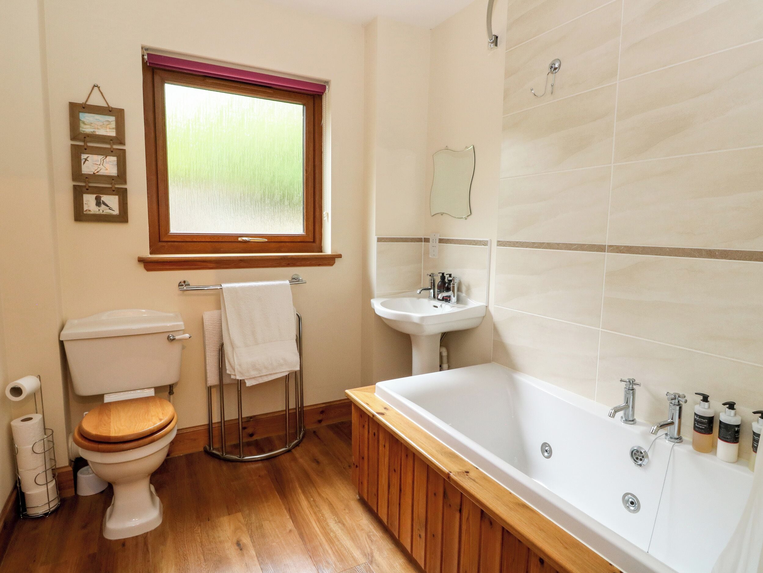 A bathroom with a toilet, sink, bathtub, wooden floor, and a window with a view.