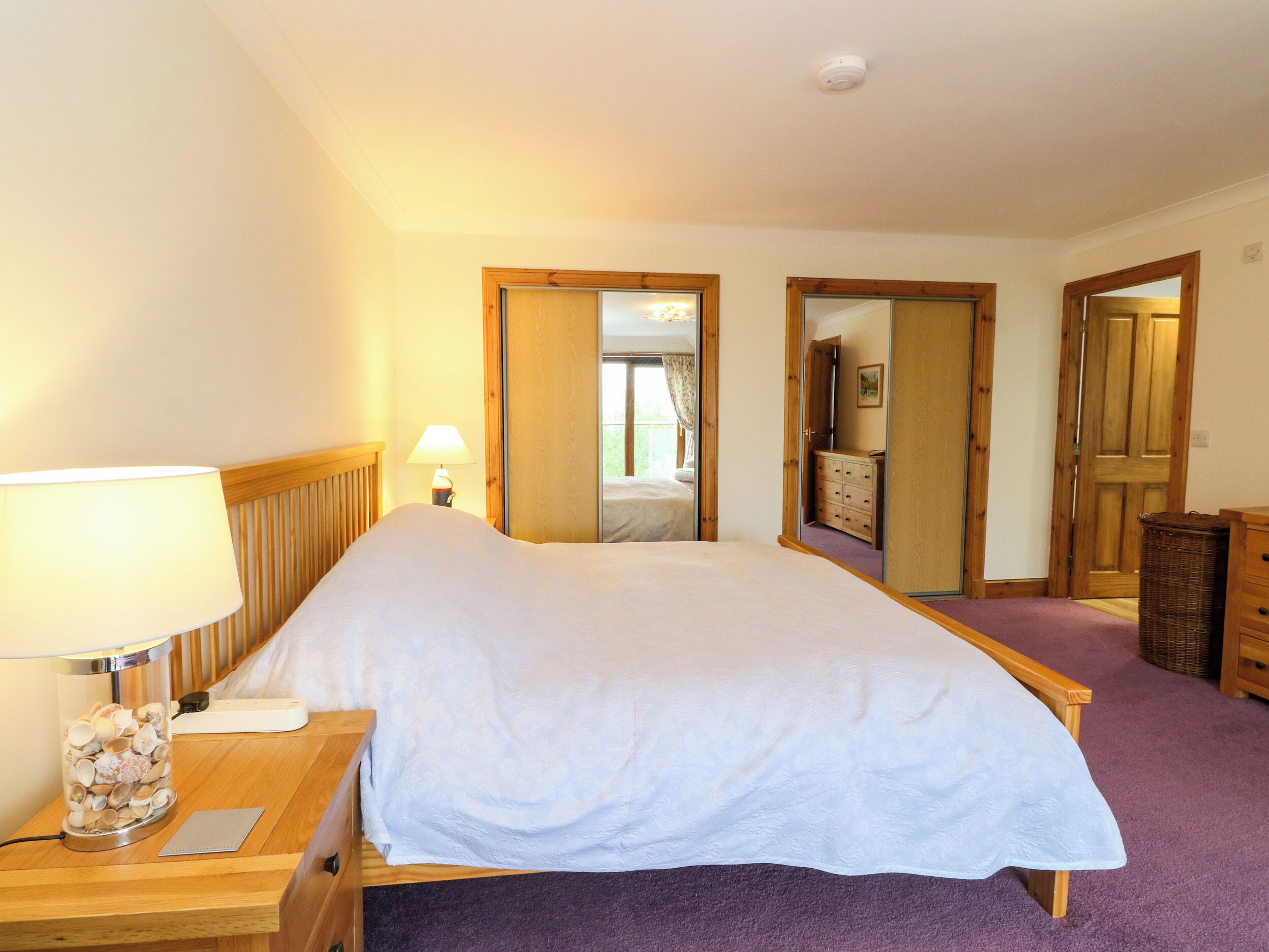 A hotel room with a bed, a nightstand with a lamp, a dresser, and a mirror.