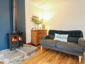 A cozy living room with a wood-burning stove, a sofa, a wooden cabinet, and a stone hearth.
