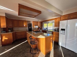 A modern kitchen with wooden cabinets, a central island, a refrigerator, and a window providing natural light.