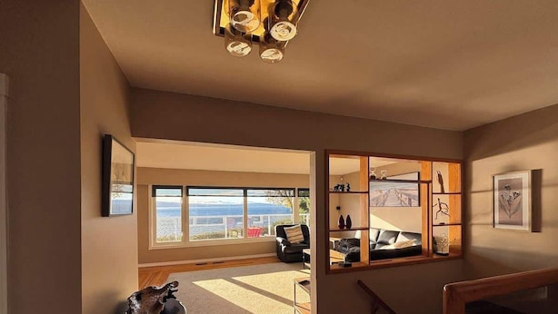 A room with a large window, a wooden floor, a black chair, and a small table with a skull decoration. - Sunset Shores Retreat (Powell River)
