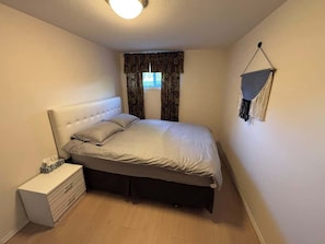 Quarto com cama, mesa de cabeceira e um painel de macramé na parede.