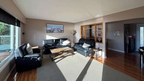 A spacious living room with a large window, a fireplace, and a wooden floor. - Sunset Shores Retreat (Powell River)