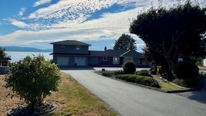 A two-story house with a garage, a driveway, and a lawn with a small tree. - Sunset Shores Retreat (Powell River)