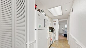 Ein schmaler Flur mit Küchenzeile, weißen Schränken, einem Kühlschrank und einer Mikrowelle.